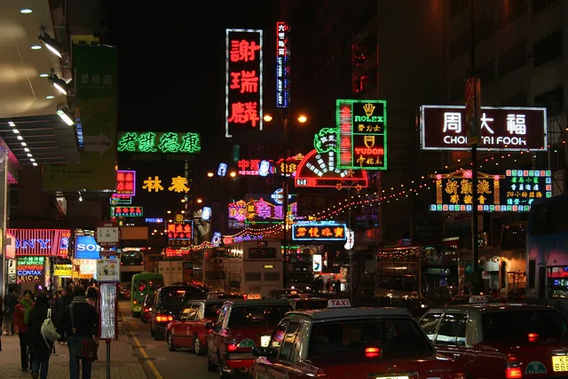 Neon shop signs glowing above traffic on Nathan Road at night in Kowloon